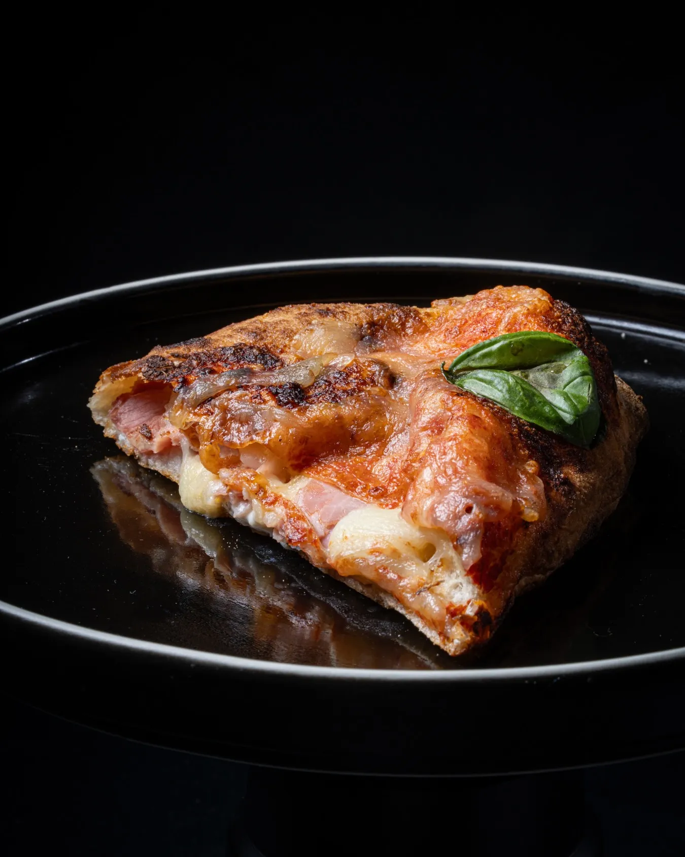 Slice of wood-fired pizza with melted mozzarella and basil on a black plate