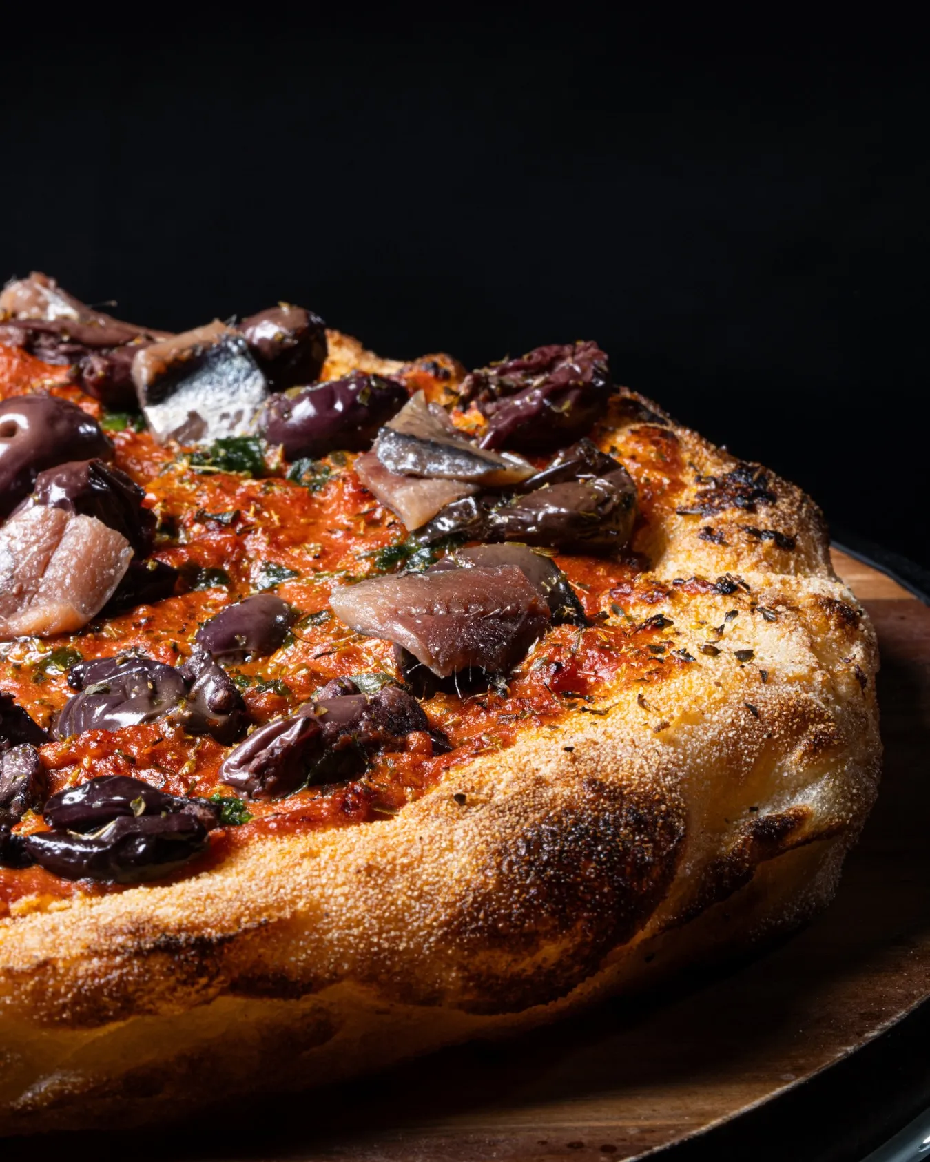 Wood-fired pizza topped with Kalamata olives and garlic on a charred crust